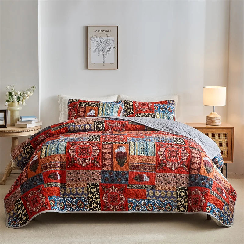 Colorful patchwork quilt on a bed in a bedroom setting with a lamp and table. Lightweight boho quilted bedspread set with pillow shams, soft all-season coverlet for queen, king, full, or twin beds in modern cloud pattern design.