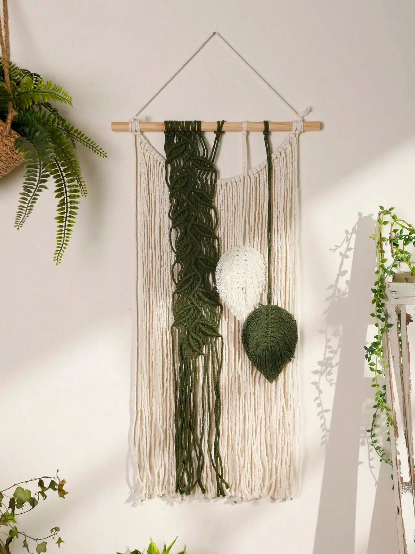 Macrame wall hanging with green and beige elements on a white wall.