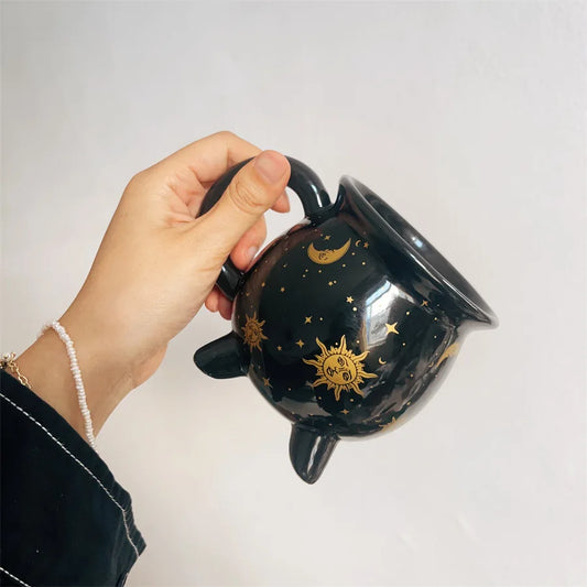 Black mug with celestial designs held by a hand against a plain background boho home decor, witch coffee mug, ceramic cauldron cup, black witch mug, Halloween kitchen decor, spooky housewarming gift, gothic home, potion mug, witchy drinkware, holiday mug for her, cozy boho kitchen accessories