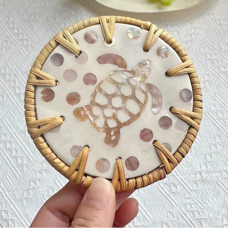 Decorative coaster with turtle design held by a hand on a textured white surface.