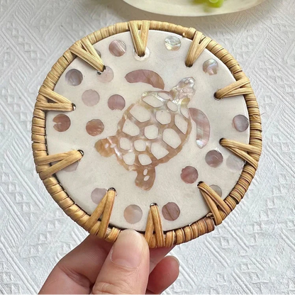 Decorative coaster with turtle design held by a hand on a textured white surface.