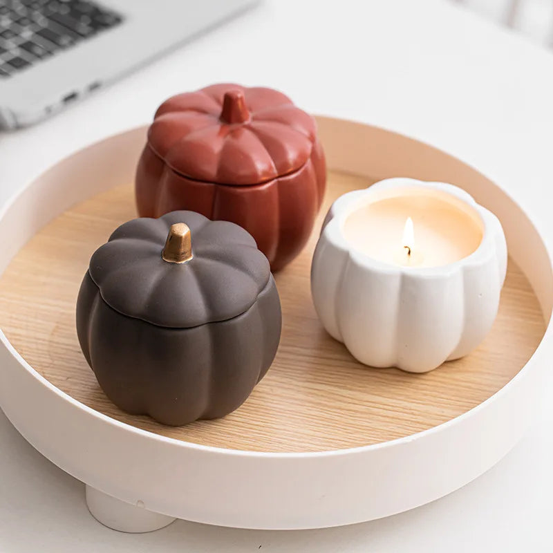 Three ceramic pumpkin-shaped containers on a wooden tray with a candle. fall home decor
