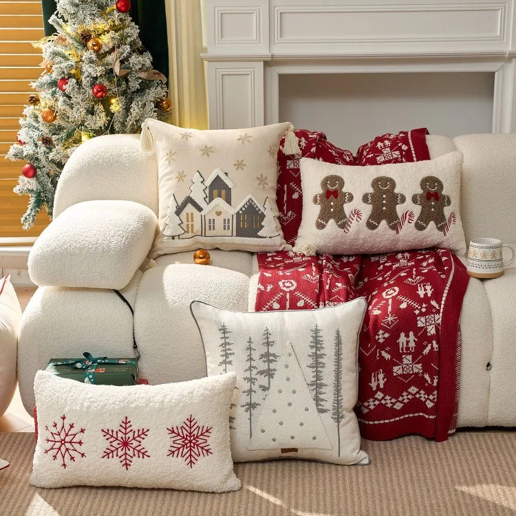 Decorative pillows with Christmas patterns on a white sofa next to a decorated tree and fireplace.