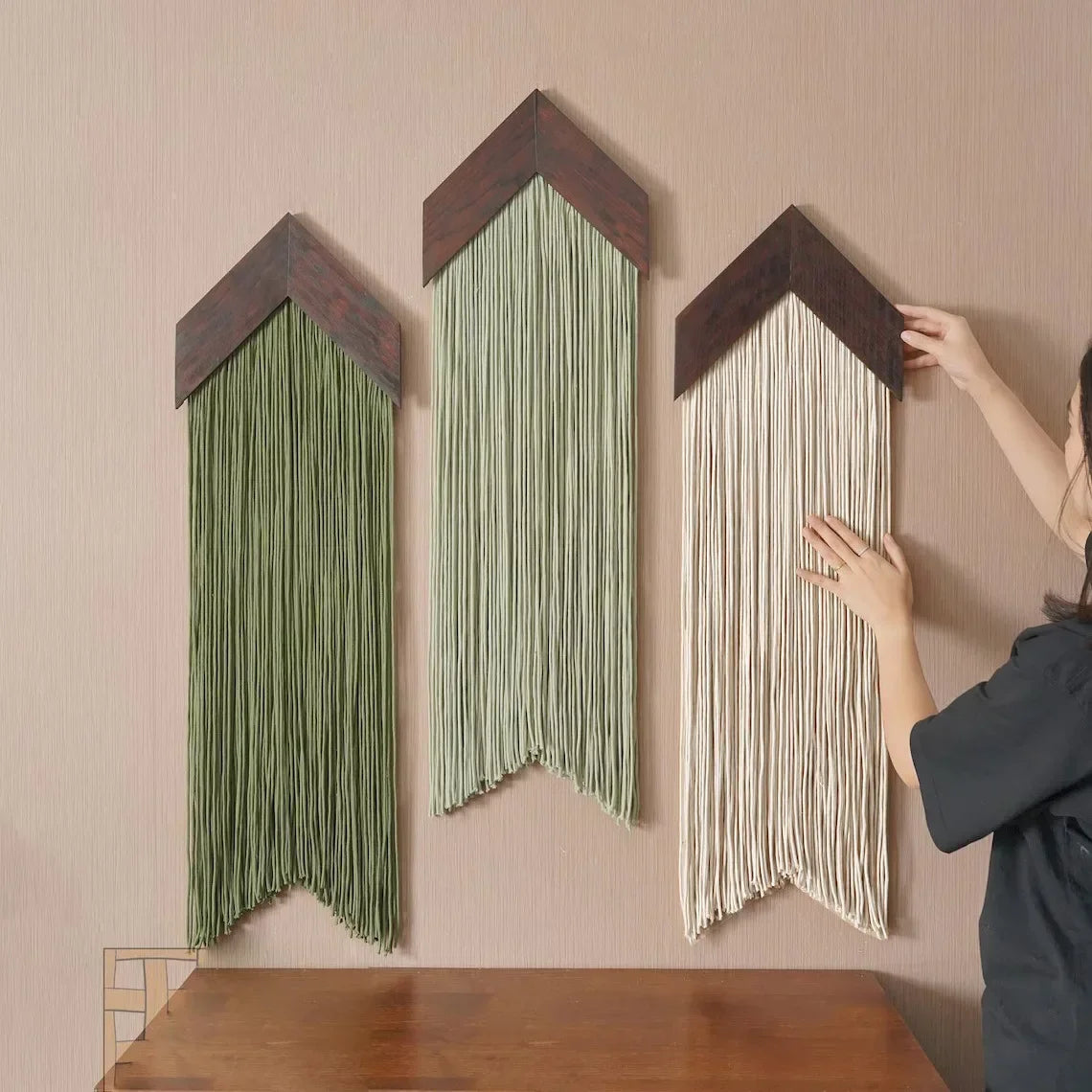Person arranging macrame art pieces on a wall