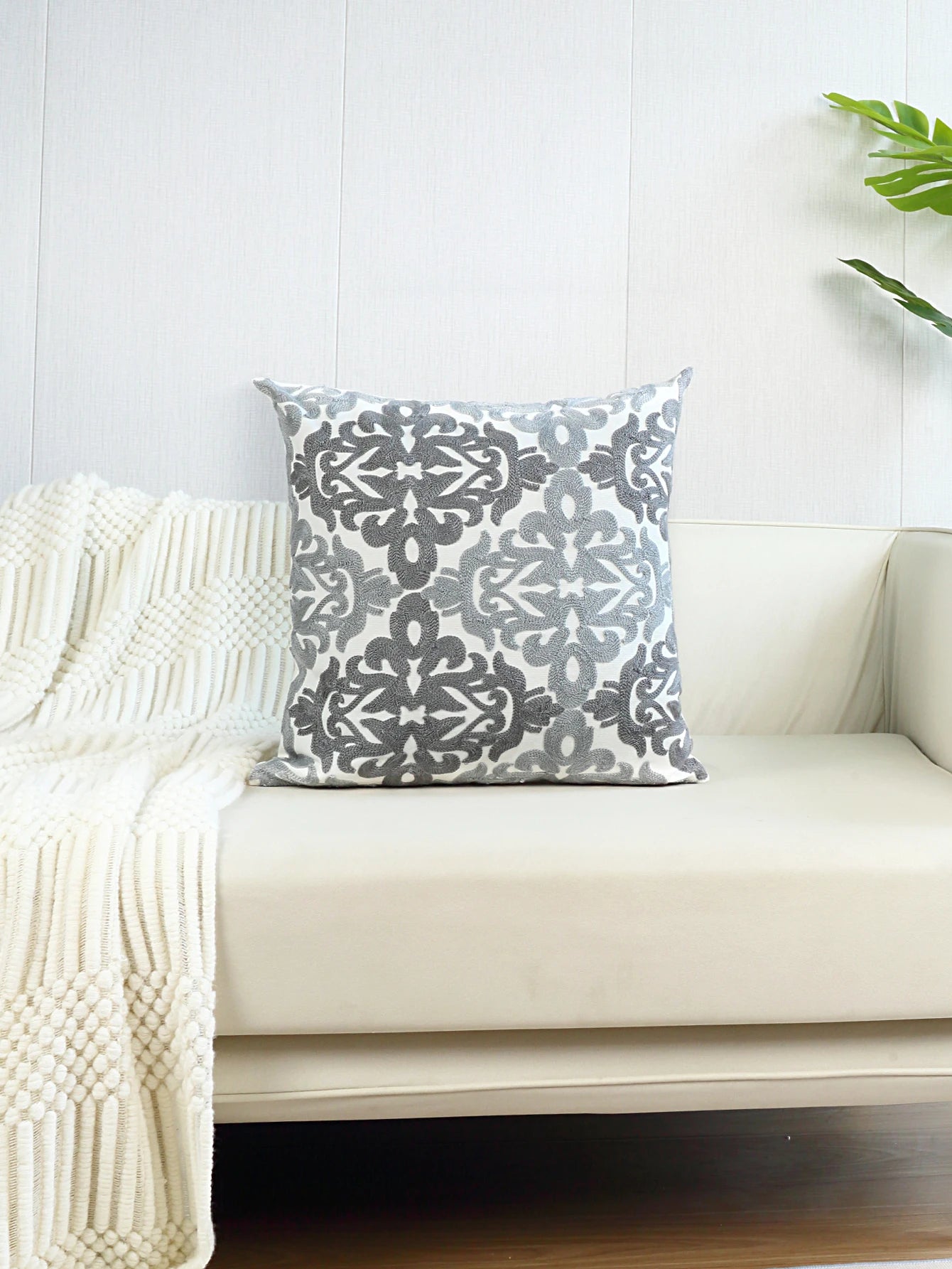 Decorative pillow with a gray and white pattern on a white couch with a white blanket.