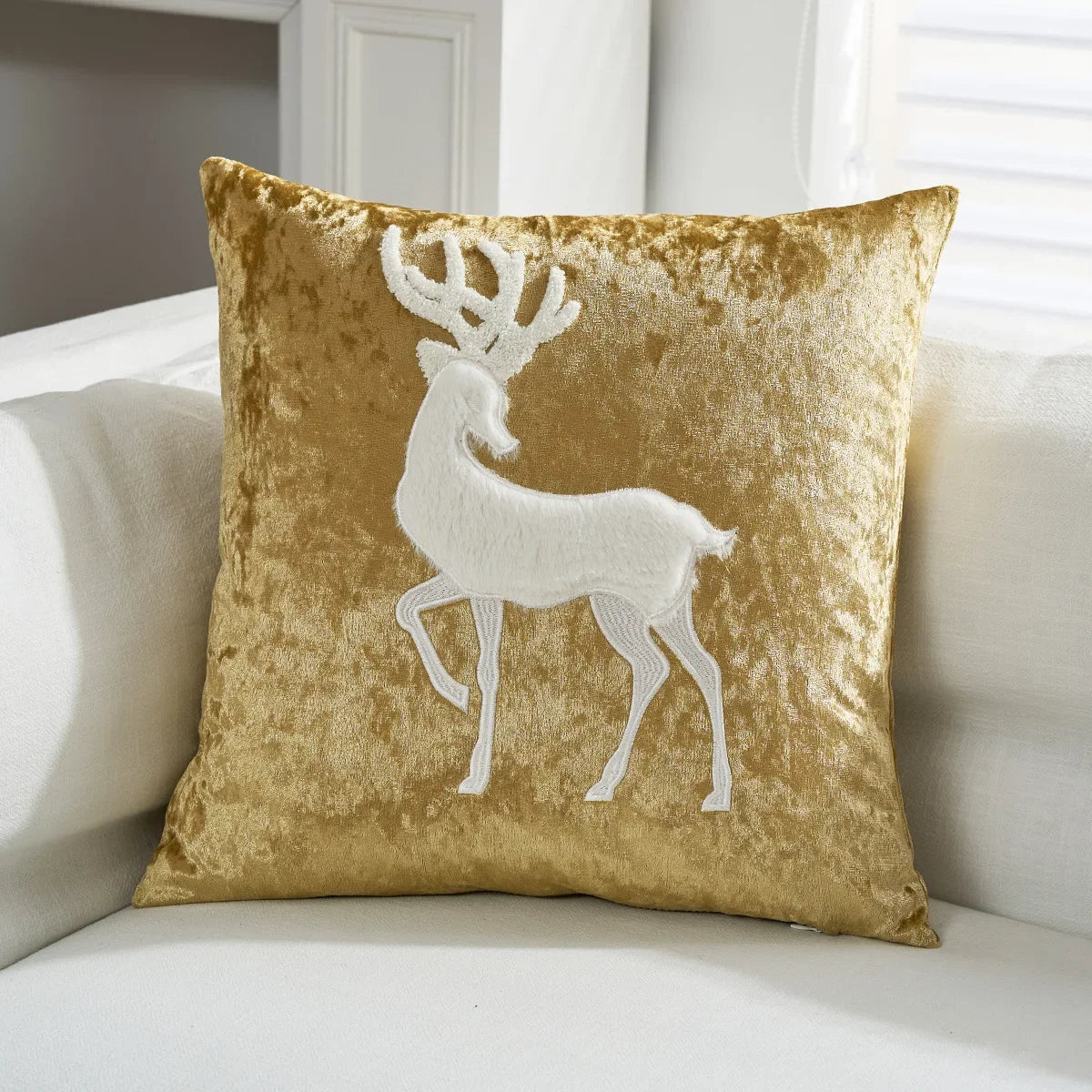Gold pillow with a white deer design on a white couch. Embroidered Merry Christmas pillow cover with snowflake design – festive red and white holiday cushion for sofa or bedroom décor.