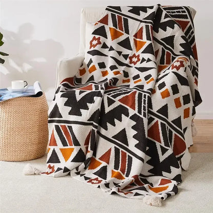 Geometric Bohemian patterned blanket draped over a chair in a room with a woven basket and plant.