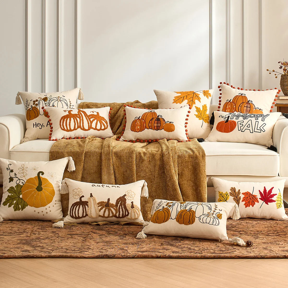 Decorative pillows with fall-themed designs on a sofa. Fall maple leaf and pumpkin throw pillow cover for Thanksgiving decor
