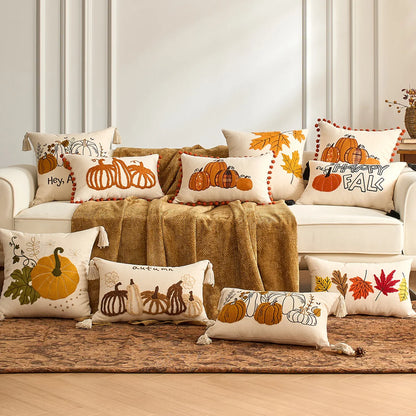 Decorative pillows with fall-themed designs on a sofa. Fall maple leaf and pumpkin throw pillow cover for Thanksgiving decor