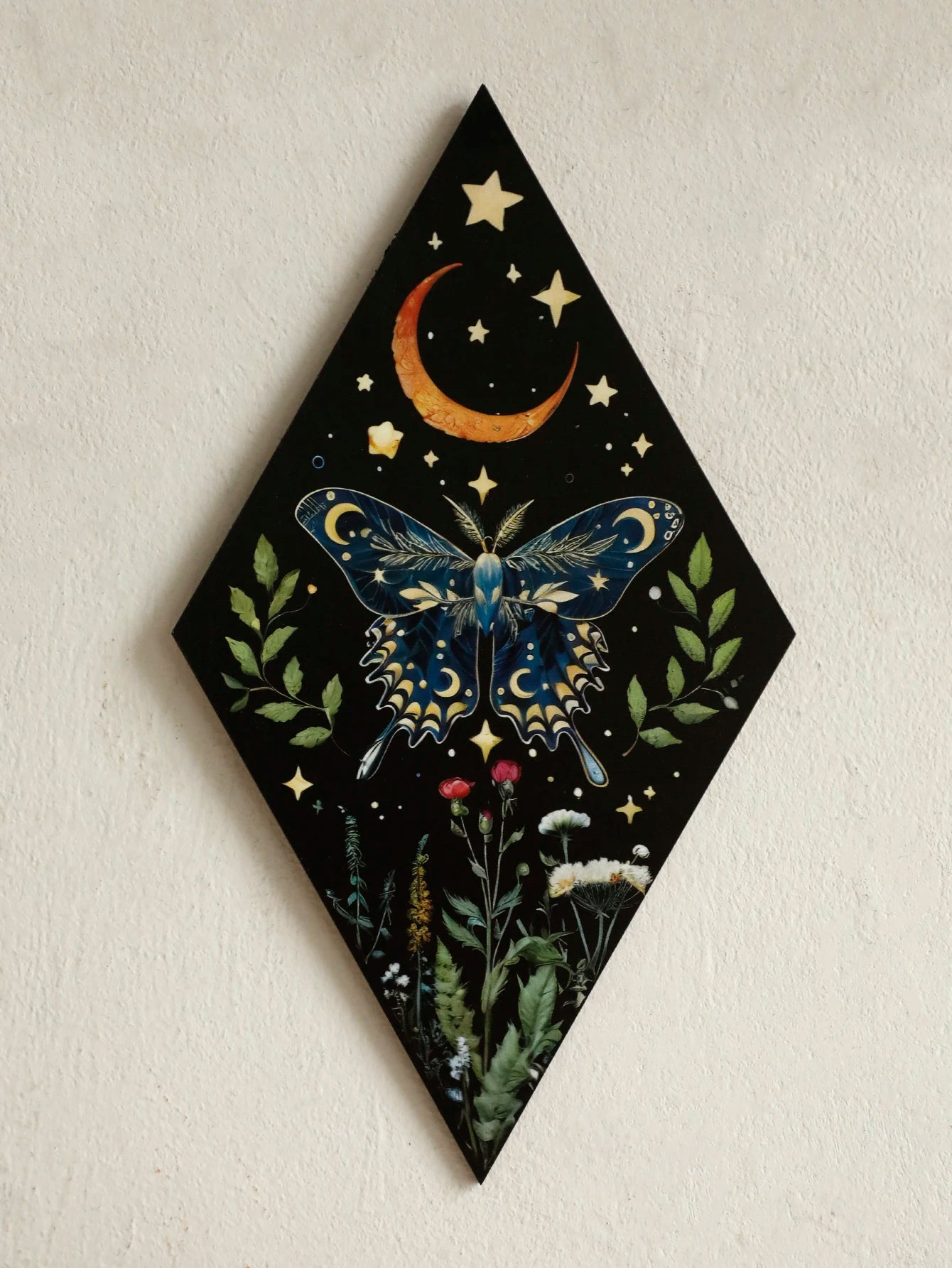 Decorative wall art with a butterfly, moon, and stars on a black diamond-shaped background. Rustic colorful wood wall art panel with moon, stars, and butterfly engraving, displayed above a sofa in a boho-styled living room