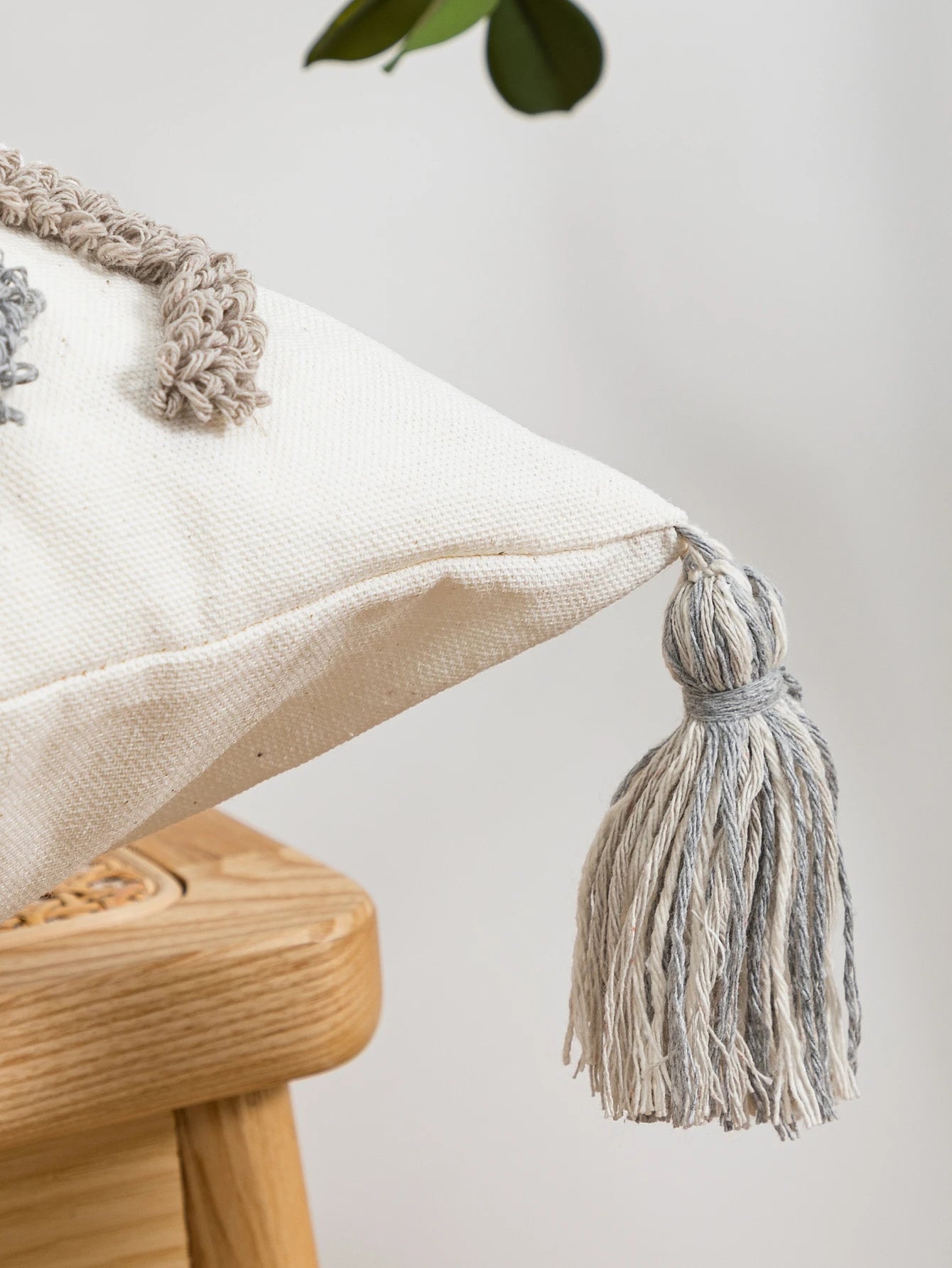 Decorative pillow with tassels on a wooden stool against a light background