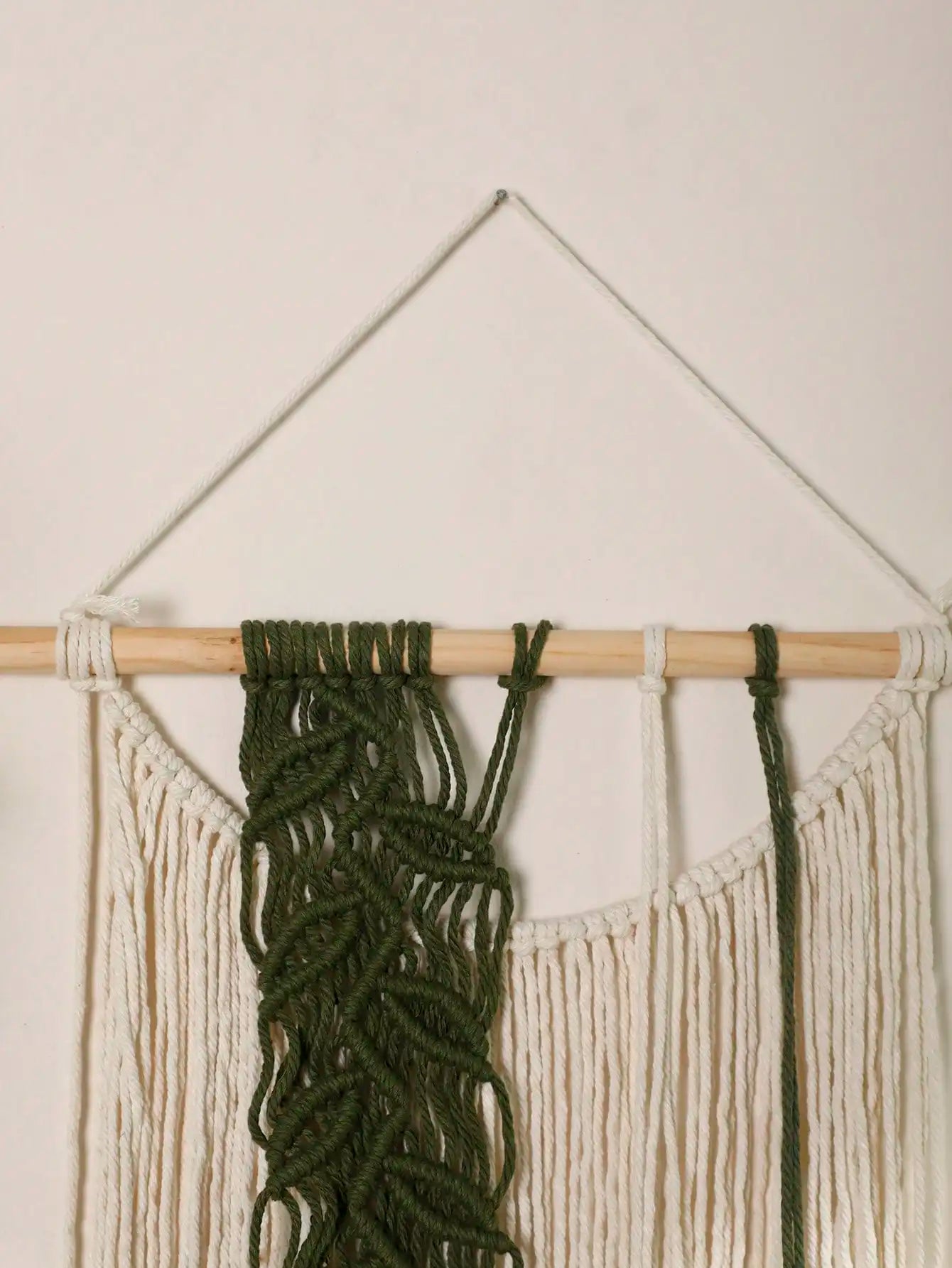 Macrame wall hanging with green and beige ropes on a white wall