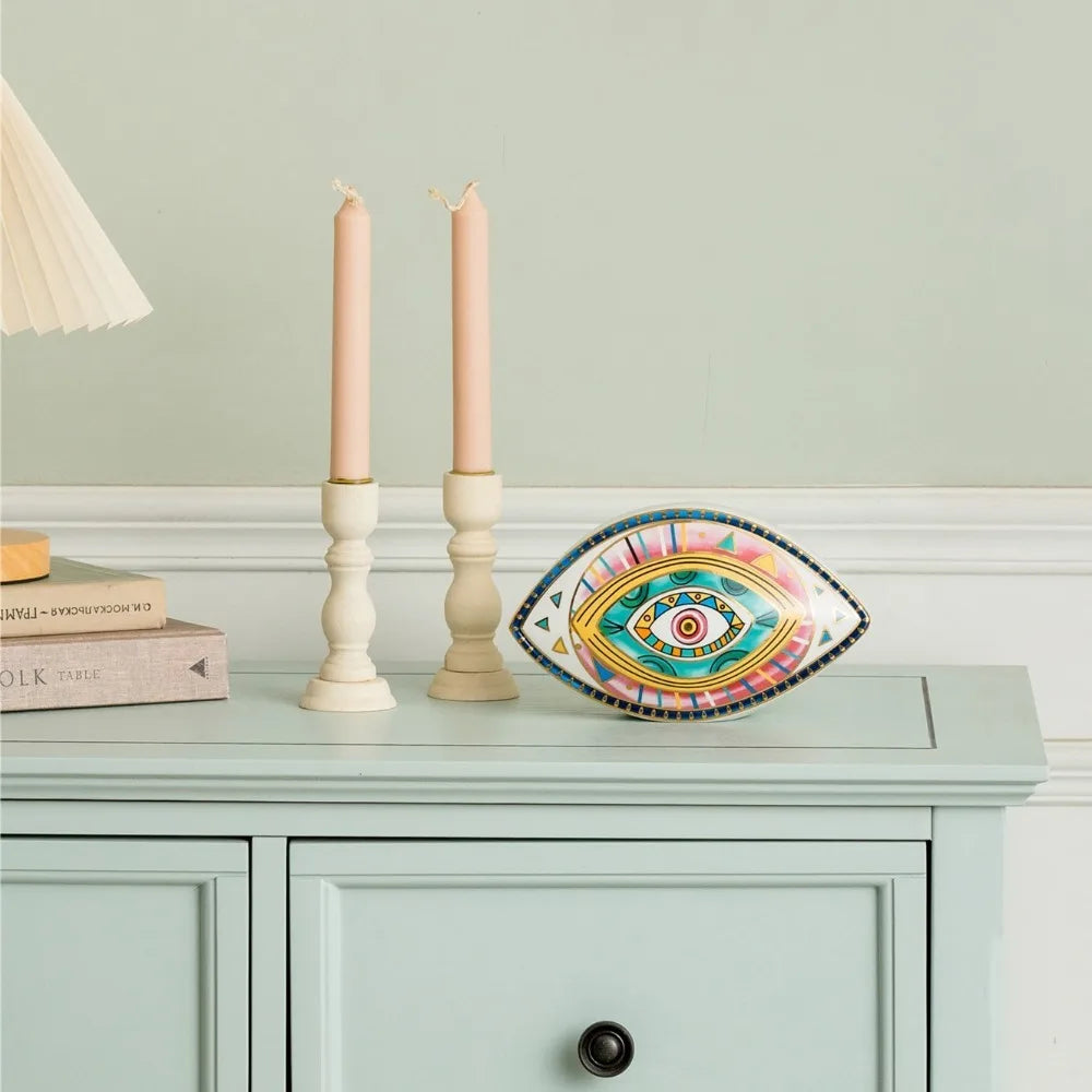 Moroccan Turkish blue evil eye ceramic figurine on display beside two candle sticks, unique bohemian home decor accent perfect for eclectic and boho home styles, adds soulful vibes and a cozy touch to any room, great for gifting as a boho home decor gift or housewarming present.
