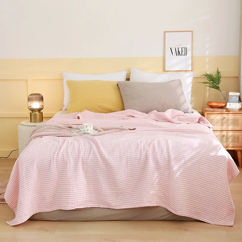 Bed with pink comforter and pillows in a bedroom setting. Boho Lightweight microfiber summer blanket for bed or sofa, cooling breathable throw for home, dorm, or office naps with geometric jacquard pattern.