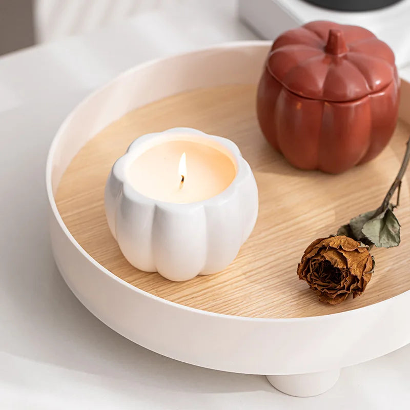 White pumpkin-shaped candle on a wooden tray with a red pumpkin and dried flower. fall home decor