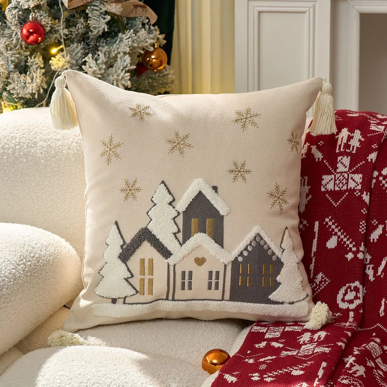 Decorative pillow with winter scene design on a couch with Christmas tree in the background