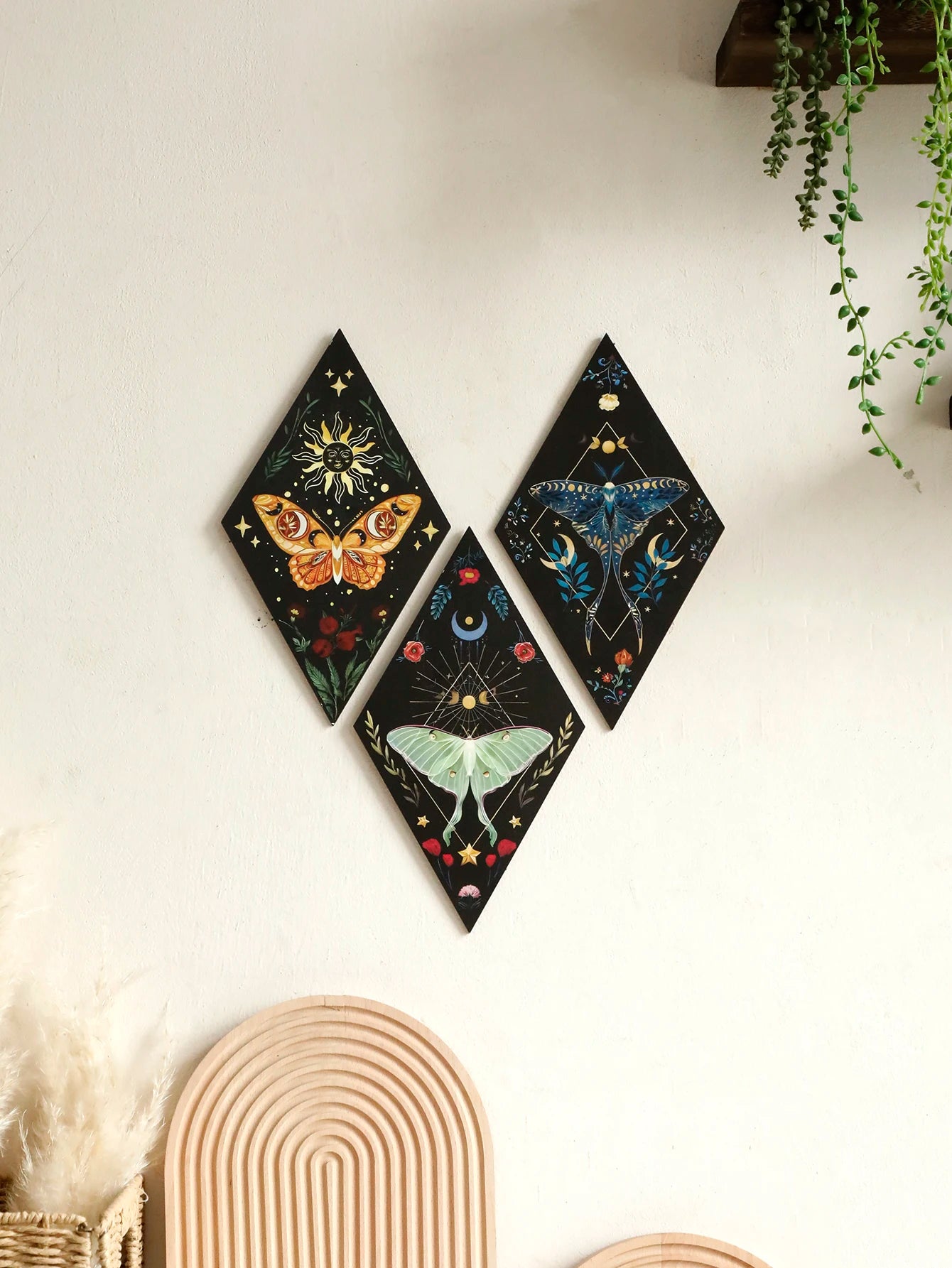 Three diamond-shaped wall art pieces with butterfly designs on a white wall. Boho wall art gift idea for housewarming or spiritual home, hanging above a cozy bedroom bed with neutral tones