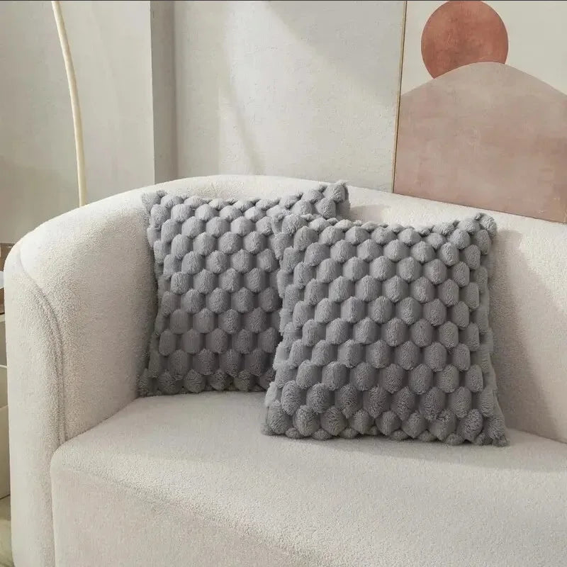 Two textured gray pillows on a beige armchair with a abstract wall art in the background.