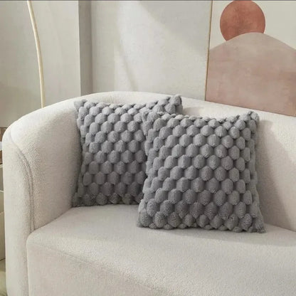 Two textured gray pillows on a beige armchair with a abstract wall art in the background.