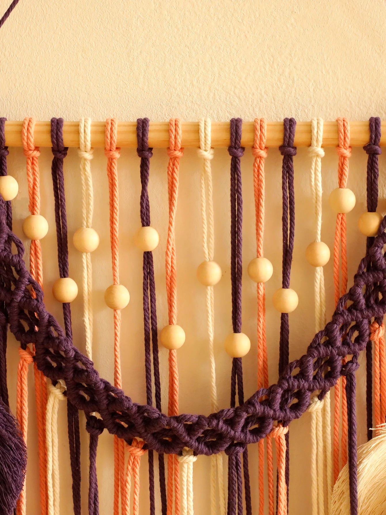 Macrame wall hanging with braided ropes and beads on a plain background