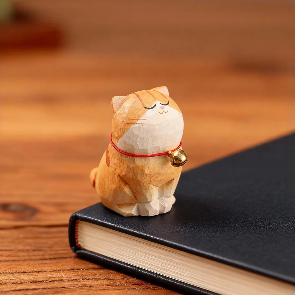 Wooden cat figurine with a bell on a black book on a wooden surface