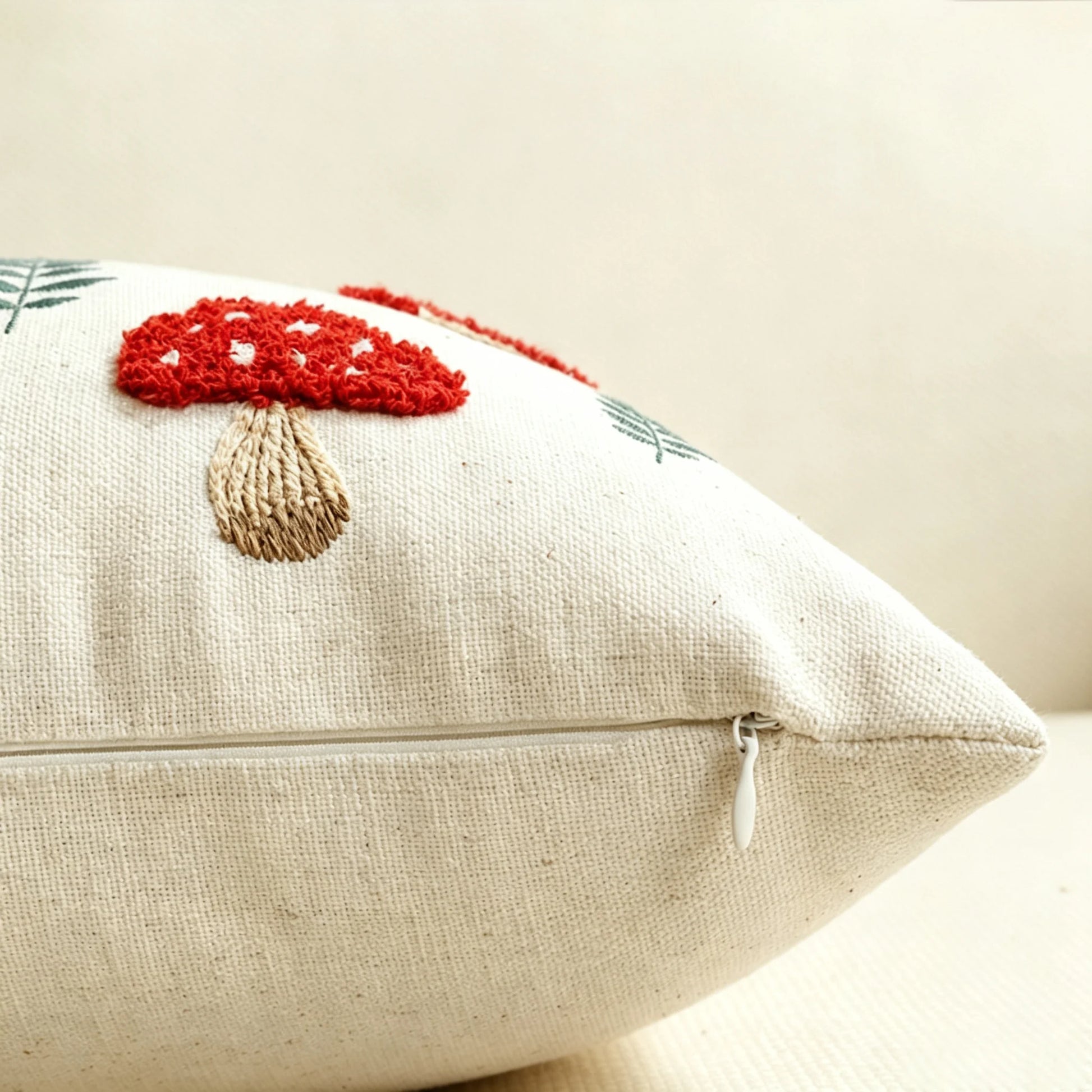 A close-up of a square beige woven throw pillow featuring a red and beige embroidered mushroom design on the front, with a visible zipper closure. Boho fall home decor.