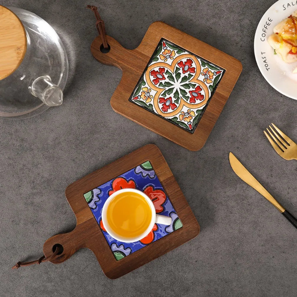 Two decorative coasters with ceramic inserts on a gray surface with a coffee cup and saucer.