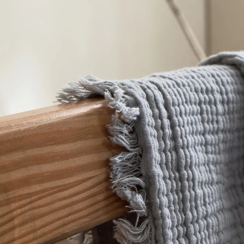 Gray textured towel draped over a wooden chair Maillard cotton gauze blanket with tassels, four-layer muslin throw for sofa, bed, and boho home decor
