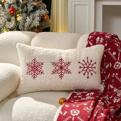 Decorative pillow with red snowflakes on a white sofa with a red blanket and Christmas tree in the background.
