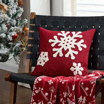 Red pillow with white snowflake patterns on a black woven chair next to a decorated Christmas tree.
