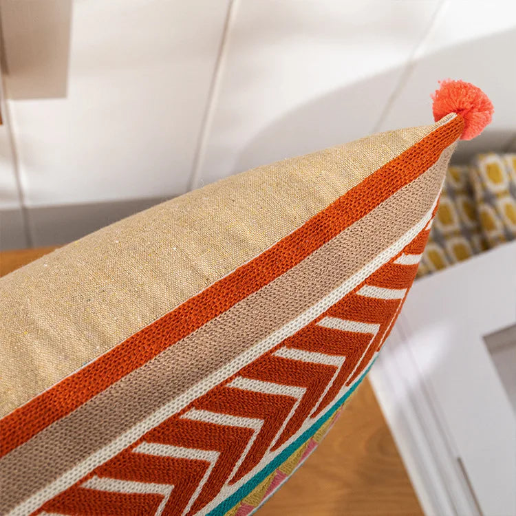 Decorative pillow with orange and beige patterns on a blurred indoor background. Bohemian embroidered throw pillow cover with geometric design, cotton-blend cushion for sofa, bed, or modern home decor.