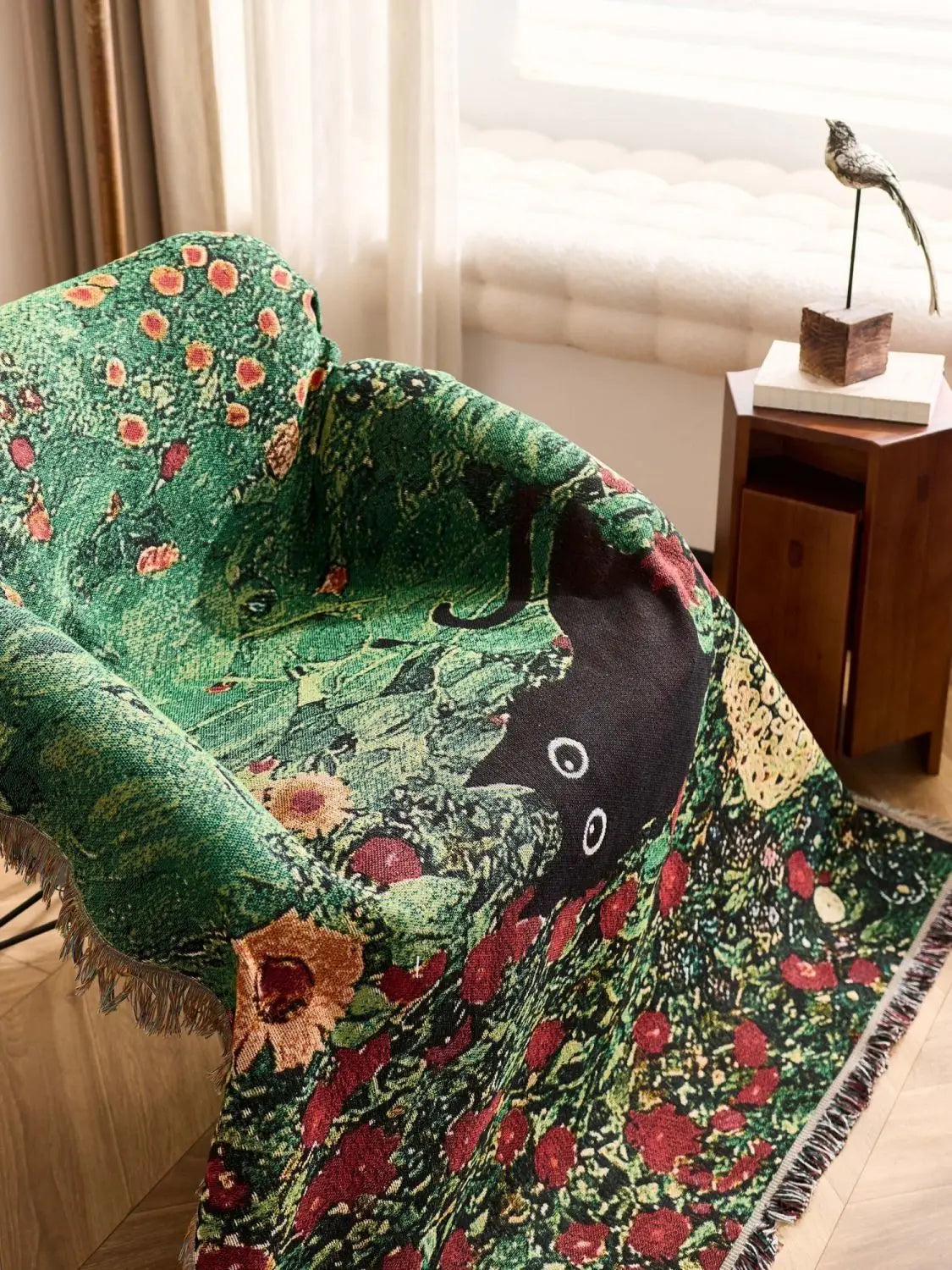 Decorative green blanket with floral patterns draped over a chair in a room. Cat woven throw blanket for boho sofa and home decor