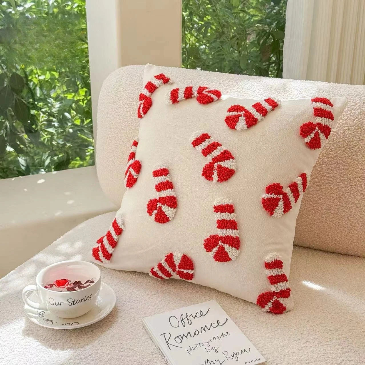 Decorative pillow with candy cane pattern on a couch next to a cup and book.
