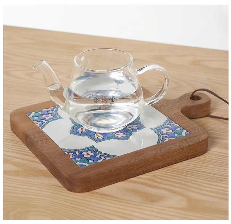 Clear glass teapot on a wooden tray with a decorative blue and white pattern