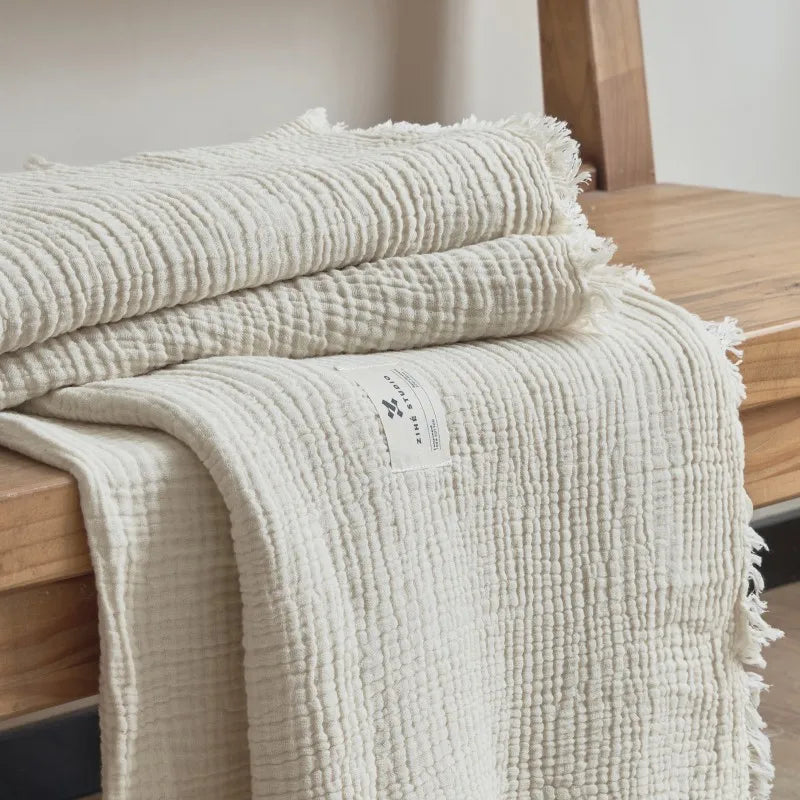 Beige textured blanket draped over a wooden surface Maillard cotton gauze blanket with tassels, four-layer muslin throw for sofa, bed, and boho home decor
