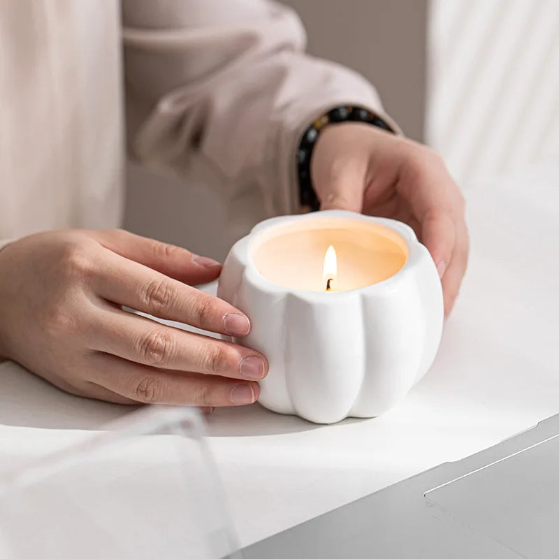 Person holding a white ceramic candle holder with a lit candle inside on a light surface. fall home decor