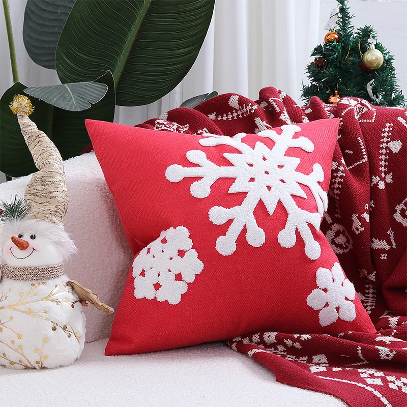 Red pillow with white snowflake patterns on a festive setting with Christmas decorations. Embroidered Merry Christmas pillow cover with snowflake design – festive red and white holiday cushion for sofa or bedroom décor.