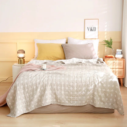 Neatly made bed with decorative pillows and a lamp in a bedroom setting. Boho Lightweight microfiber summer blanket for bed or sofa, cooling breathable throw for home, dorm, or office naps with geometric jacquard pattern.