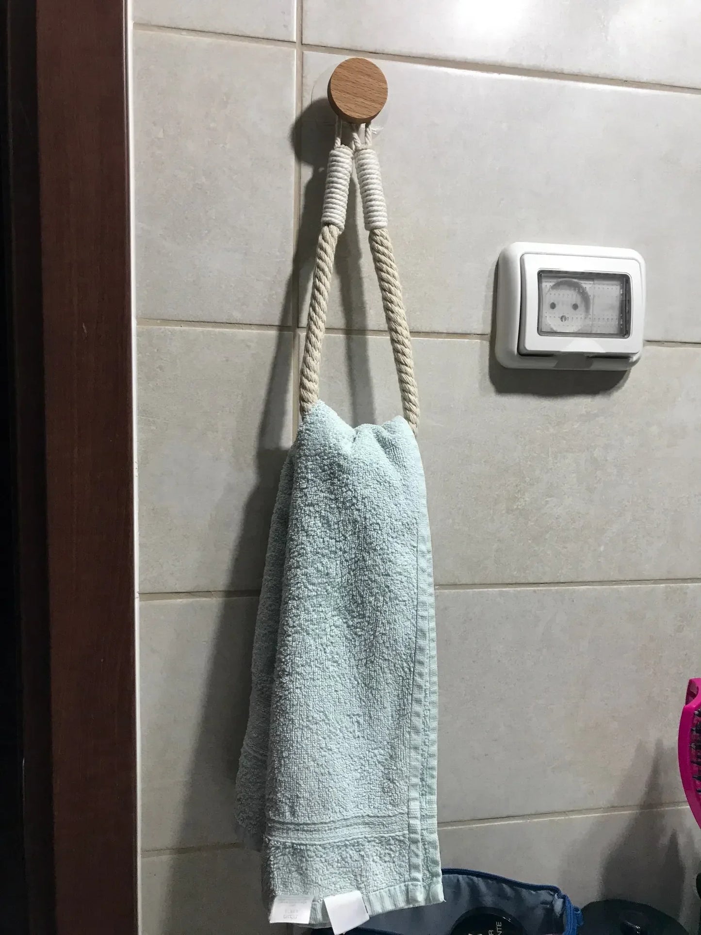 Green towel hanging on a wooden hook against a tiled wall. Boho rope toilet paper holder, nail-free wall mounted paper towel rack, rustic bathroom storage and decor accessory with wood and rope design