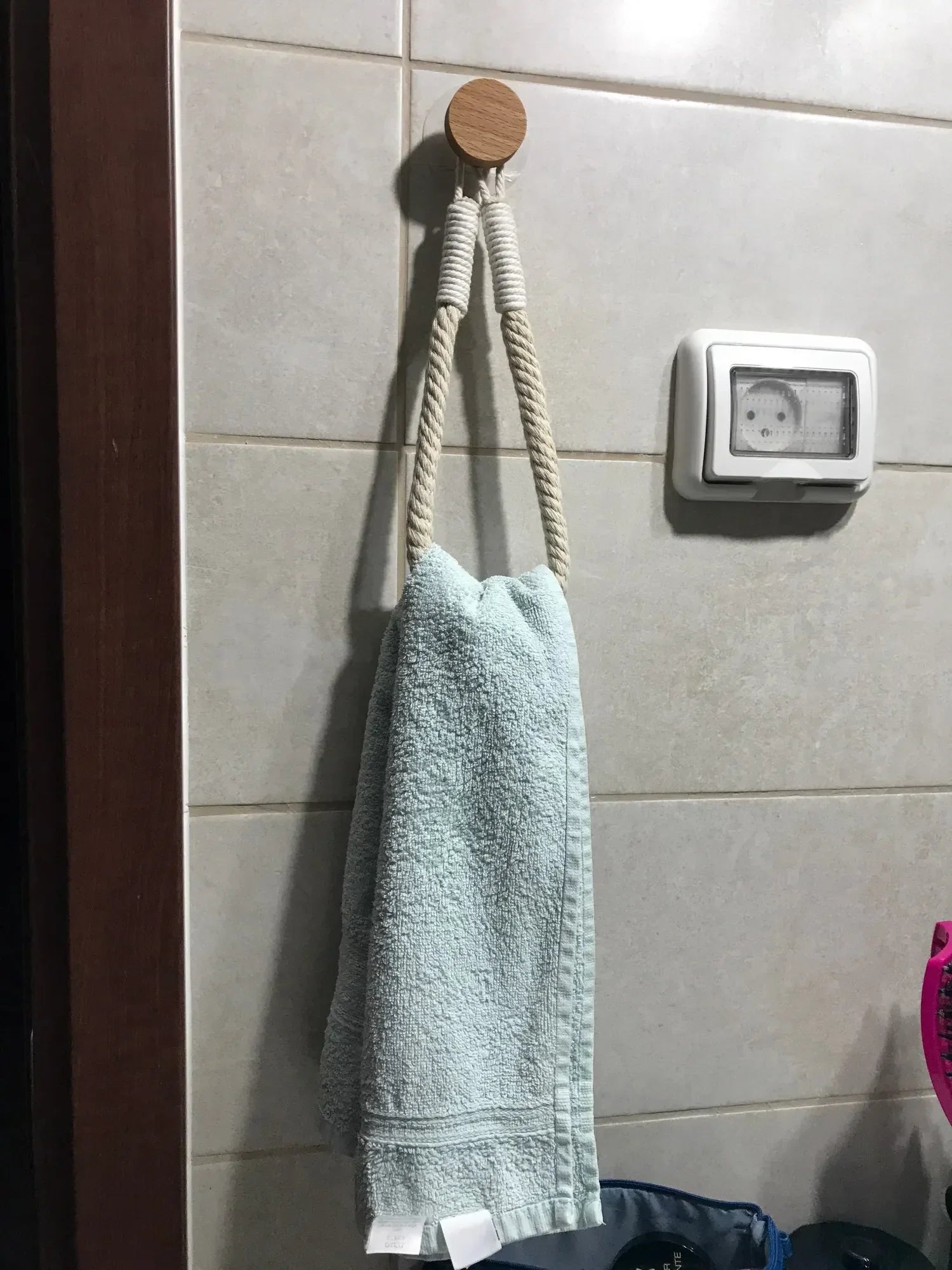 Green towel hanging on a wooden hook against a tiled wall. Boho rope toilet paper holder, nail-free wall mounted paper towel rack, rustic bathroom storage and decor accessory with wood and rope design