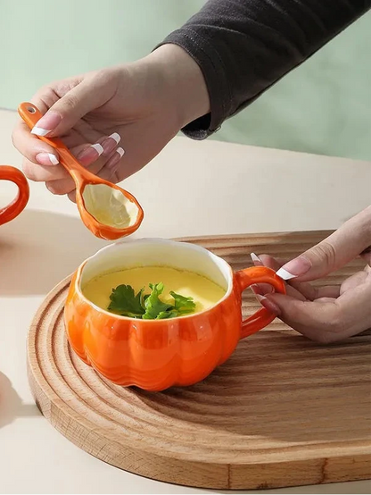 Person holding an orange pumpkin-shaped mug with soup and a measuring spoon, on a wooden surface. Pumpkin ceramic mug with spoon Halloween autumn fall coffee cup