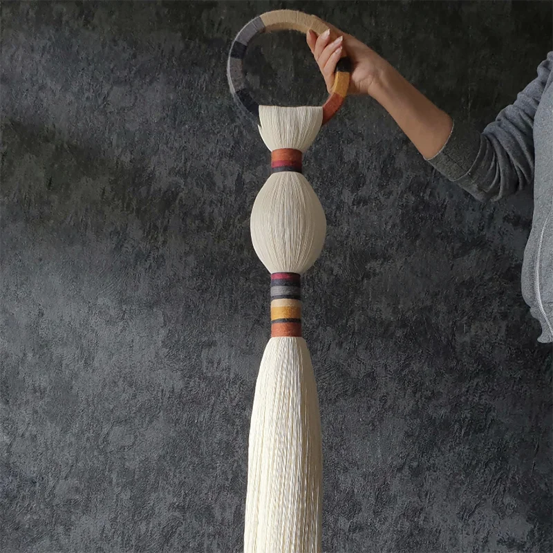 Decorative tassel held by a hand against a dark background. boho macrame wall art