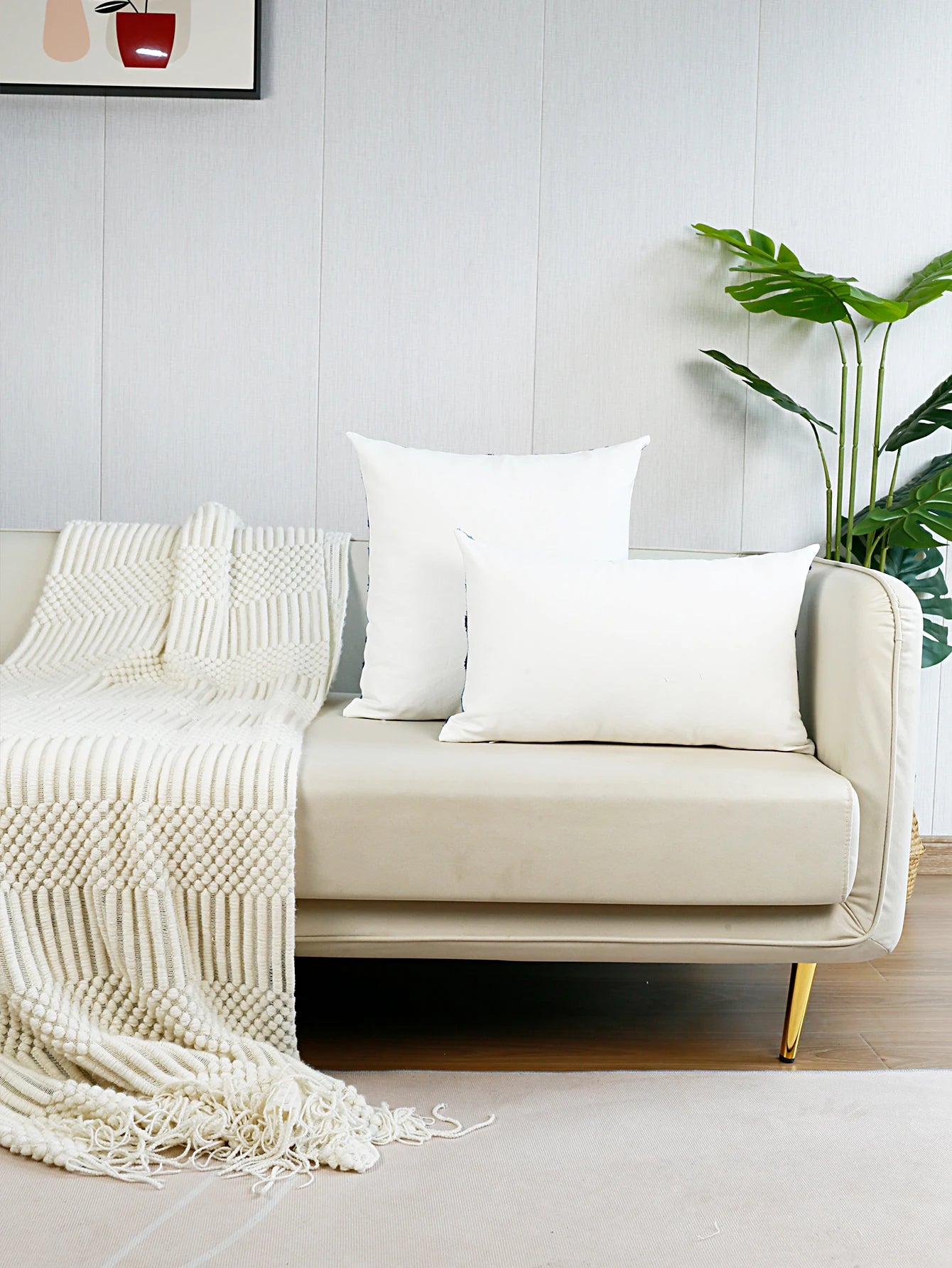 Beige sofa with white pillows and a blanket in a minimalistic living room.