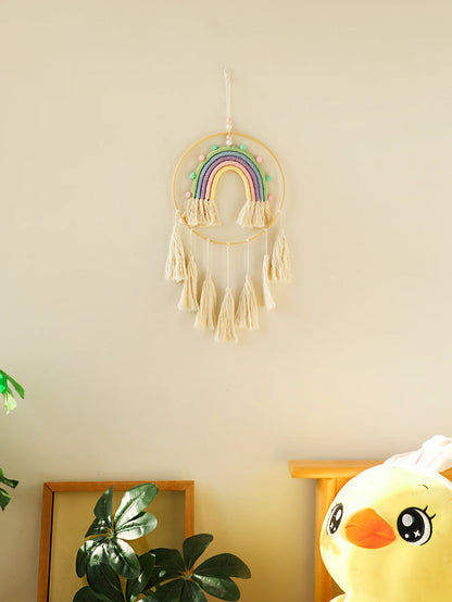 Decorative rainbow dreamcatcher hanging on a wall with a yellow plush toy and plant in the foreground. Handmade macrame rainbow wall hanging boho home decor