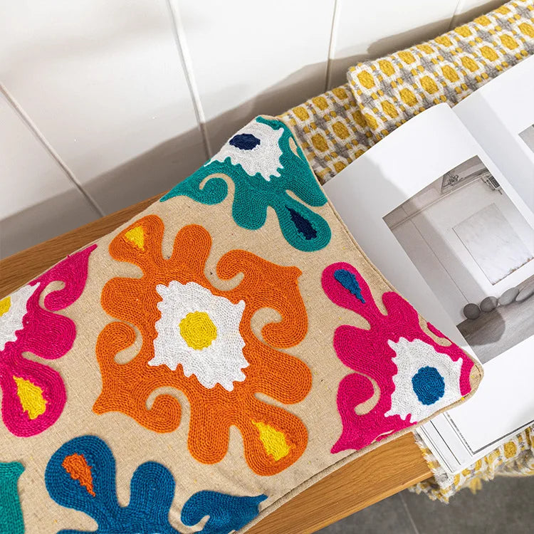 Colorful floral-patterned rug on a wooden floor with a white wall in the background. Bohemian embroidered throw pillow cover with geometric design, cotton-blend cushion for sofa, bed, or modern home decor.