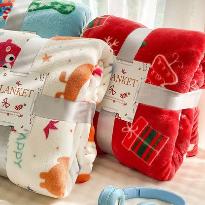 Three folded blankets with labels on a light surface, one red with reindeer design, one white with orange fox design, and one multicolored.