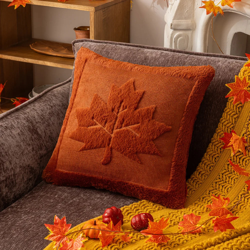 Orange pillow with leaf design on a gray couch, surrounded by autumn decorations. Halloween pumpkin plush pillow cover for sofa and bed decor.