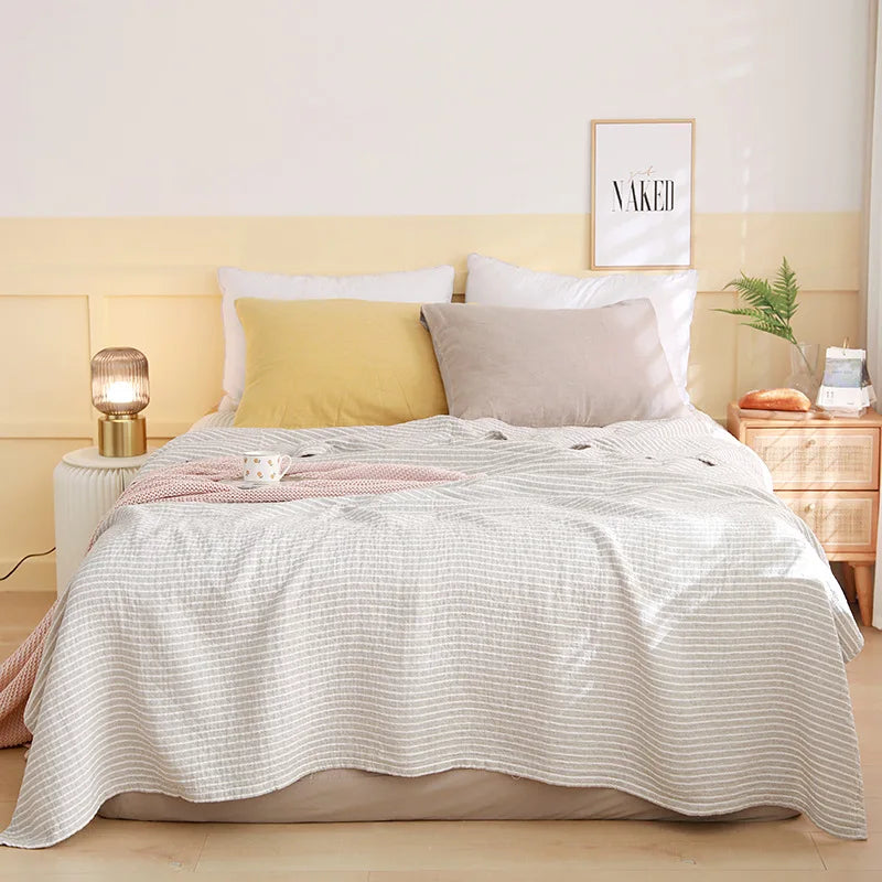 Bedroom with a neatly made bed featuring a white quilt, yellow and gray pillows, and a lamp on a nightstand. Boho Lightweight microfiber summer blanket for bed or sofa, cooling breathable throw for home, dorm, or office naps with geometric jacquard pattern.