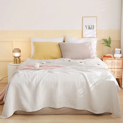 Bedroom with a neatly made bed featuring a white quilt, yellow and gray pillows, and a lamp on a nightstand. Boho Lightweight microfiber summer blanket for bed or sofa, cooling breathable throw for home, dorm, or office naps with geometric jacquard pattern.