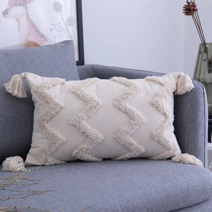 Decorative pillow with tassels on a gray sofa in a living room setting.